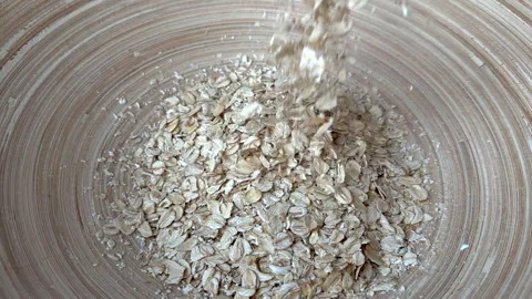 Oat flakes grain falling into a bamboo bowl Stock Footage 244384864