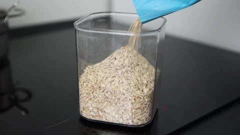 Oats flakes pouring transparent container black countertop modern kitchen Vidéo 328980158
