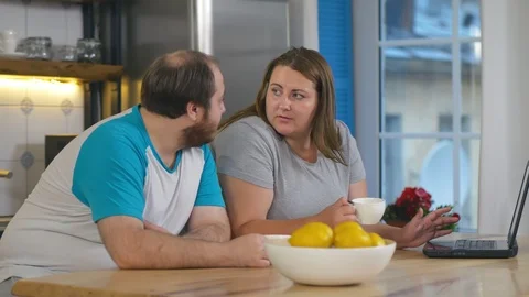 Obese couple having breakfast at the kitchen, looking at laptop computer Stock Footage 124657814