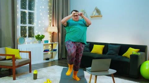 An obese man is on a blue workout mat in a living room, he is doing front kicks Video stock 166449517