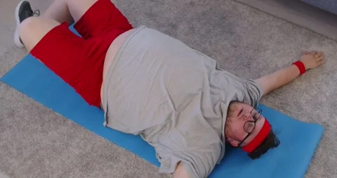 Obese man doing physical exercise, lifting leg with turn to side at home, top Stock Footage 329719229