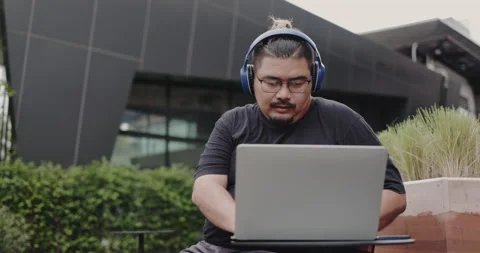 Obese man wearing headphone to work and video call with laptop meetings outside  Stock Footage 159724311