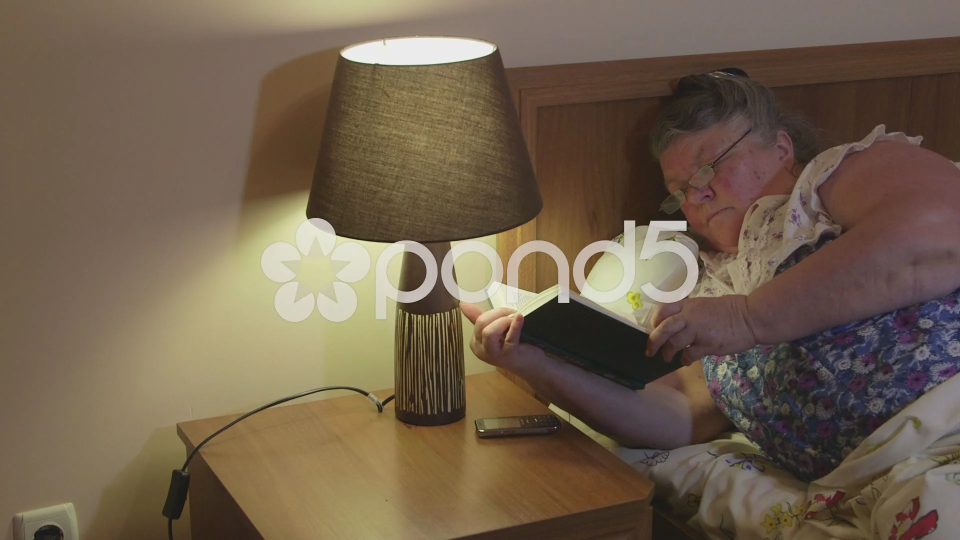 Obese old woman lying in bed at home reading book