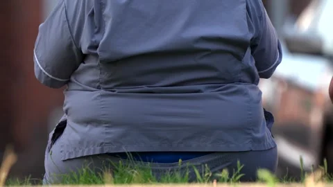 An obese person sat down while people walk past in a town centre Stockbeeldmateriaal 281788497