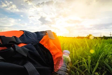 Object of backpack with water bottle on sunset and green grass view. Stock Photos