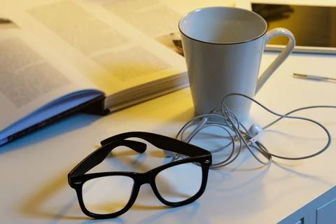 Objects on the desk - Cup of hot drink, spectacles, books and earphones Stock Photos