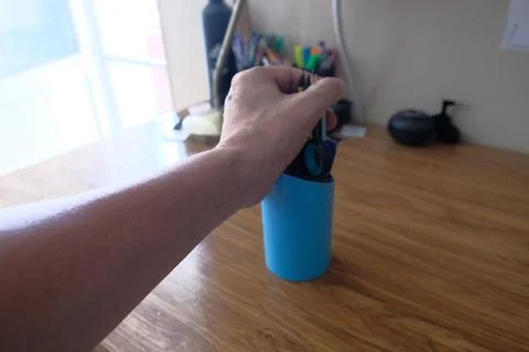 Objects in a persons hand: a flask, pens and pencils Stock Photos