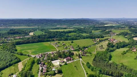 Oblique aerial view pulling back over rural village, patchwork farmland, winding Stock Footage 342359334