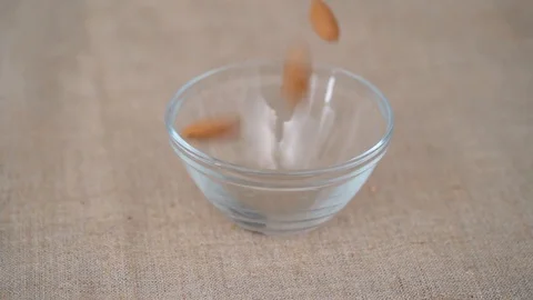 Oblong and nutritious almonds fall into a transparent plate.  Video stock 113701225
