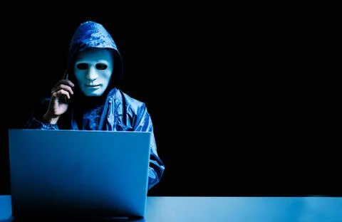 Obscured dark face using laptop computer for cyber attack and calling cellphone Stock Photos