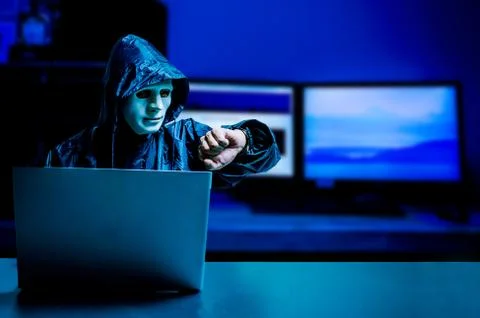 Obscured dark face using laptop computer for cyber attack and checking time Stock Photos