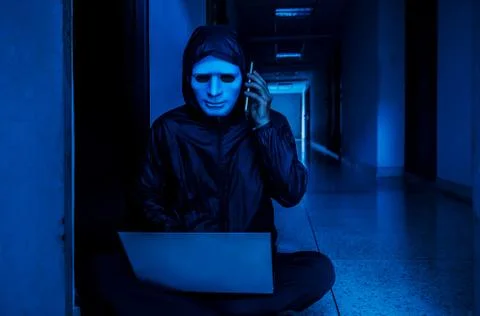 Obscured dark face using laptop computer for cyber attack and calling Stock Photos
