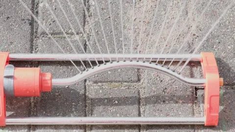Observe the functioning of a garden sprinkler system spraying evenly on a paved Video stock 326633373