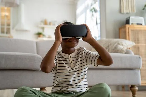 Obsessed child black boy experiencing 3D virtual reality in VR goggles sits at Stock Photos