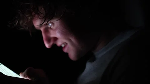 Obsessed man smiles while staring at glowing phone screen in darkness showing si Video stock 313842918