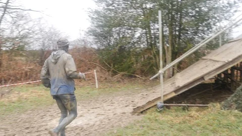 An obstacle course racer runs through mud and approaches an obstacle Stock Footage 112006302