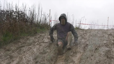 An obstacle course racer slides down a muddy hill 動画素材 112004450