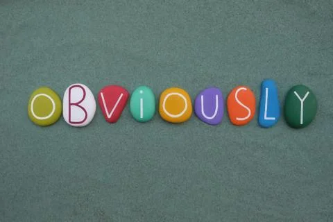Obviously, english word composed with multicolored stone letters over green sand Stock Photos