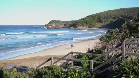 An ocean bay beach with a serfer walking towards the shore. Stock Footage 134578074