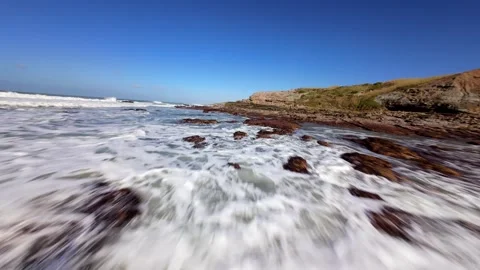 Ocean crashes against jagged, weathered rocks under bright sun Stock Footage 346077444