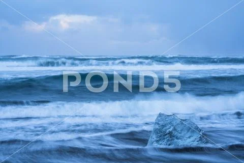 The ocean crashes around a chunk of ice on the South shore of Iceland near Jokul Stock Photos