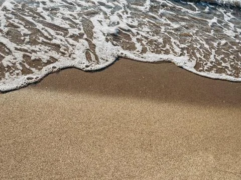 Ocean foam gently touching smooth brown sand surface in minimalist seashore.. Foto stock