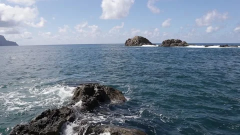 The ocean gently crashes against the rocks of the coastline of a volcanic i.. Stock Footage 228256155