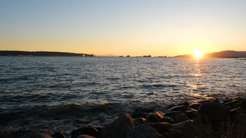 Ocean harbor at sunset. Ships on the horizon. Waves splashing on the rocky beach Stock Footage 252246960