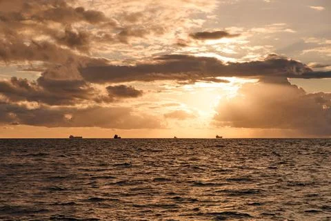 Ocean horizon glows beneath dramatic clouds at golden sunset Stock Photos