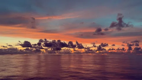 The ocean reflects the vibrant colors of a sunset sky with clouds 動画素材 338282732
