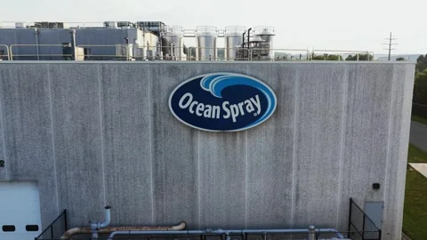 Ocean Spray logo marks weathered gray industrial wall beneath rooftop storage Stock Footage 340970692