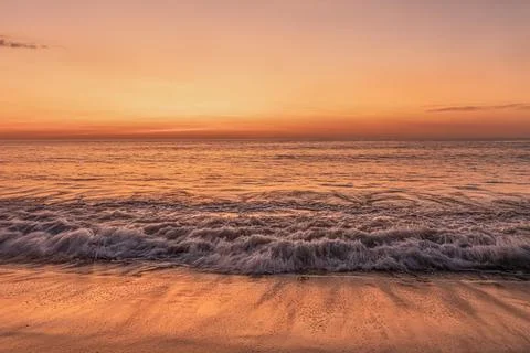 Ocean sunset with waves on sandy beach, calm sea and warm evening light, na.. Foto stock