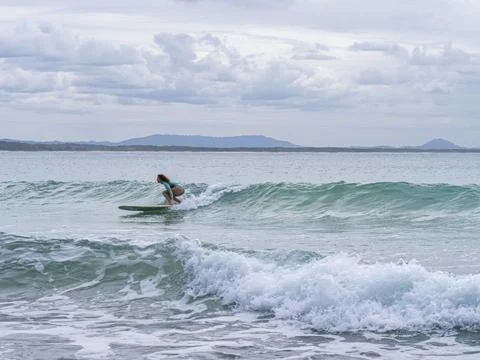 Ocean surfer maneuvers through breaking wave under overcast sky Stock Photos