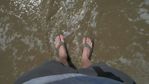 Ocean Tide Waves wash over Male feet wearing flip flops, gray shorts on Stock-Footage 280221901