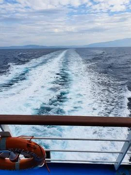 Ocean Wake Behind a Ship With Deck Railing and Lifebuoy Overlooking Distant Stock Photos