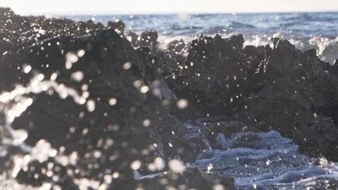 Ocean water splashes against dark rocky coast in bright sunlight Stock Footage 337410230
