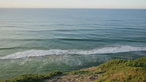 Ocean water waves make their way towards shore in Portugal cliff as sun sets Stock Footage 289678125