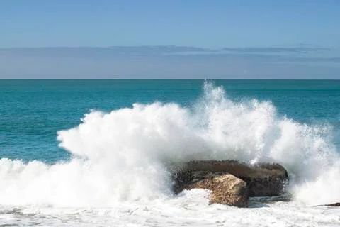 Ocean wave breaking in splash over rock on the beach Stock Photos
