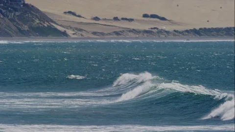 Ocean wave breaking on a windy day with sand dunes in the background Vídeo Stock 119186005