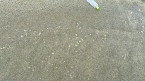 Ocean wave carrying plastic bottle from sandy beach into sea. Plastic pollution Stock Footage 337410669