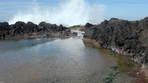 An ocean wave crashing over rocks, and the water flowing into  a tidepool Stock Footage 80546471