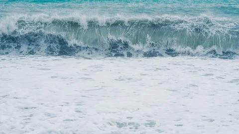 Ocean wave crashing on sandy beach with foam and turquoise water Stock Photos