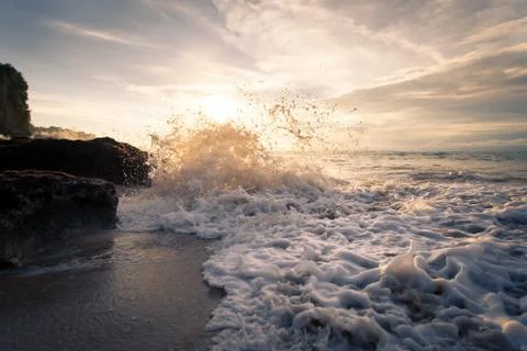 Ocean wave with foam beating against the rocks at sunset Foto stock
