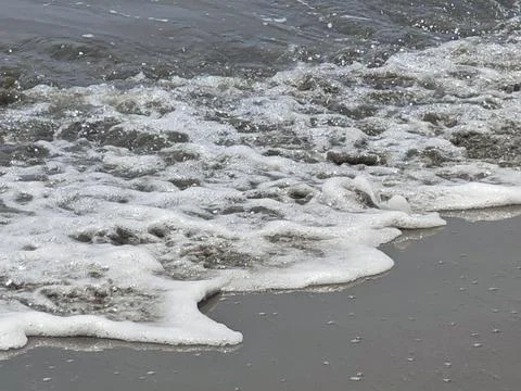 Ocean wave foam washes onto sandy beach shore surface texture Stock Photos