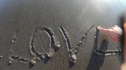 Ocean wave under light of sun washes away inscription Love POV 스톡 동영상 154368631