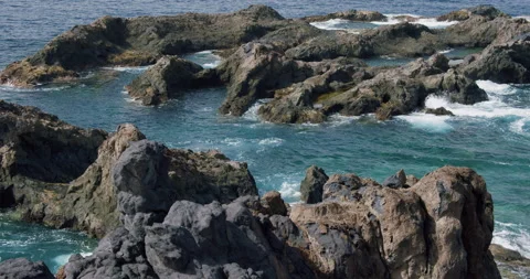 Ocean wave water lapping washing black rock stone close up with light reflection Stock Footage 192048120