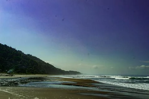 Ocean Waves Along the Coast with a Distant Green Hill Under Blue Sky Stock Photos