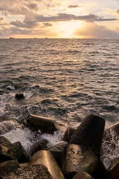 Ocean waves break over coastal concrete blocks at golden sunset Stock Photos