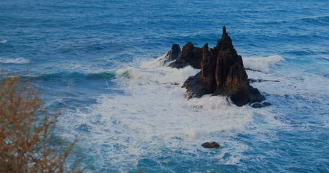 Ocean waves break on the rocky volcanic coast forming air foam on a sunny day Stock Footage 200469450