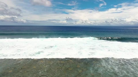 Ocean waves breaking over a reef beneath a cloudy blue sky Stock Footage 341327932